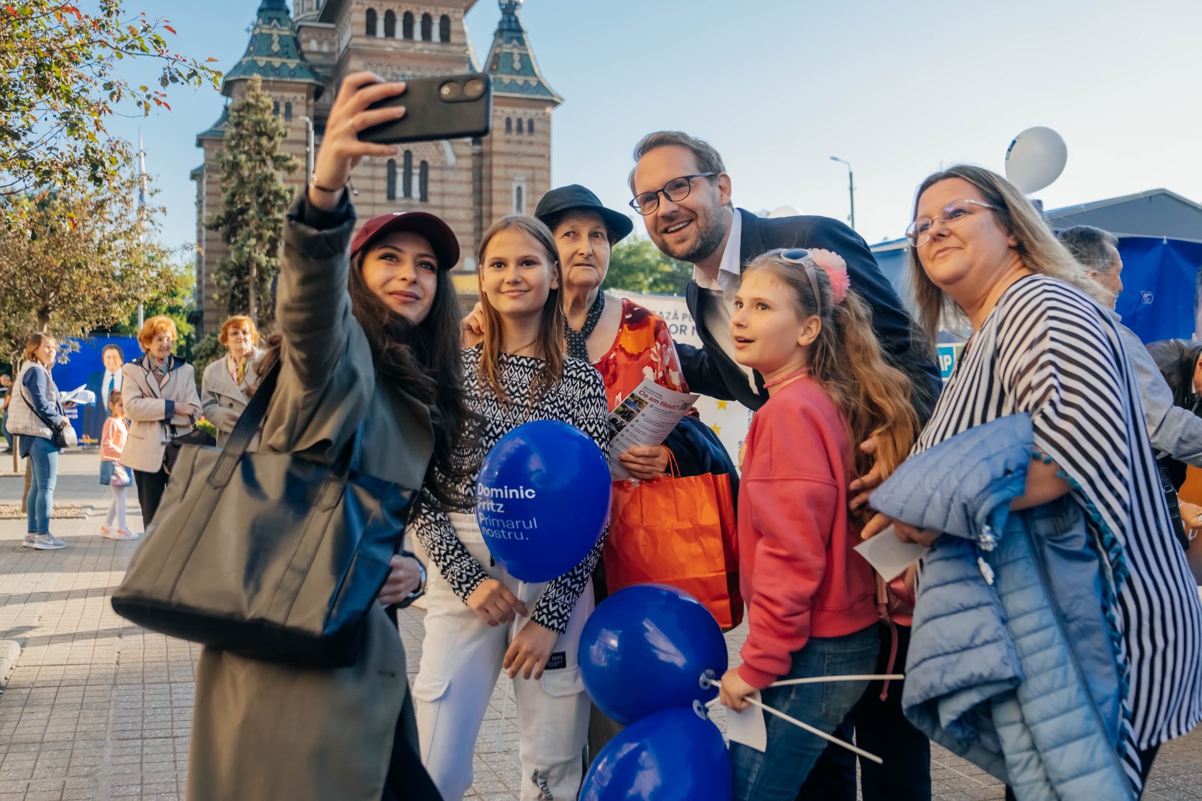 Dominic Fritz posing for a selfie with residents of Timișoara, the Orthodox Cathedral behind them