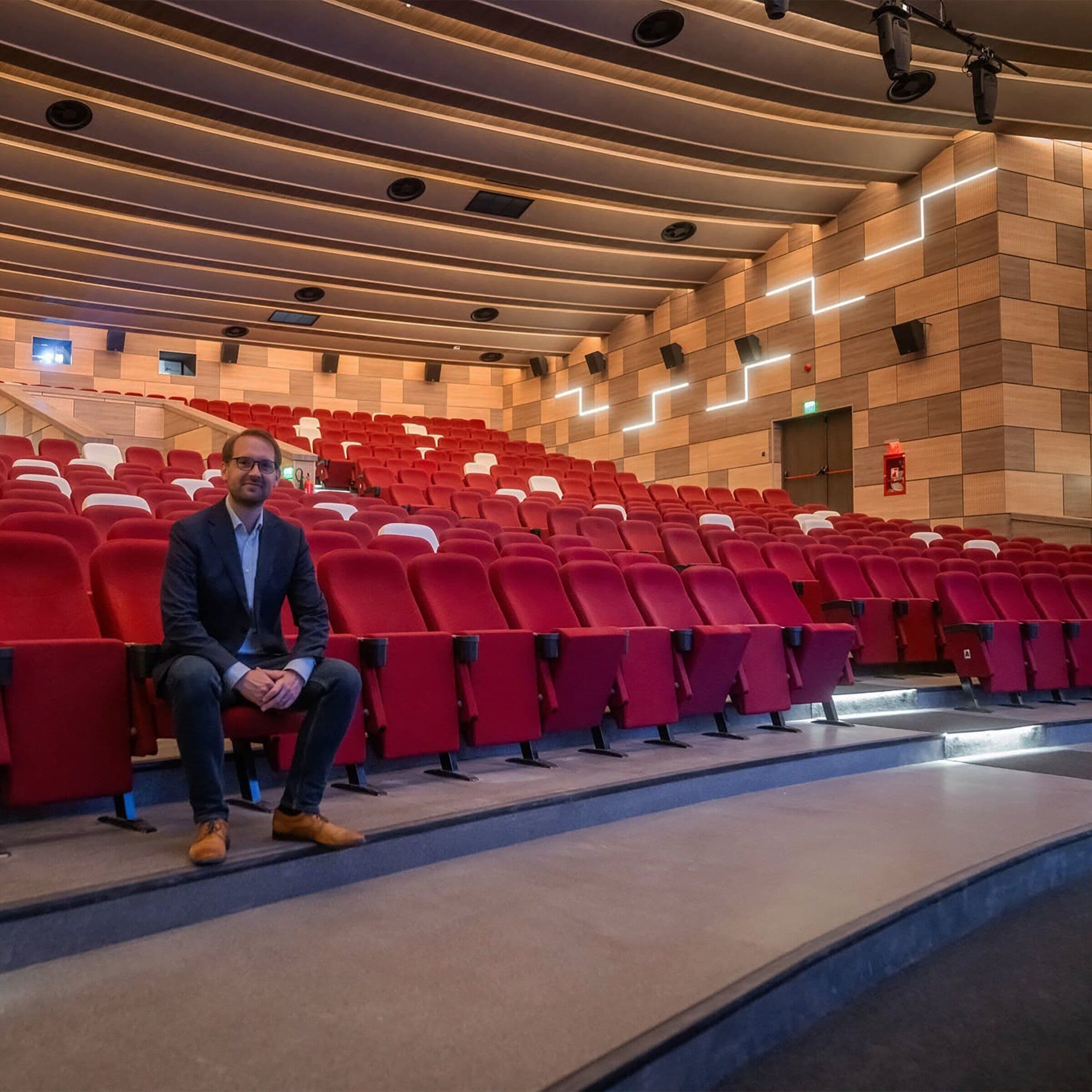 Dominic Fritz așezat într-o sală de cinema renovată, cu scaune roșii