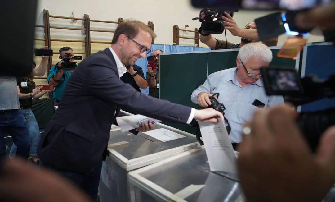 Dominic Fritz putting his ballot paper into the ballot box at a polling station, surrounded by television cameras and photographers