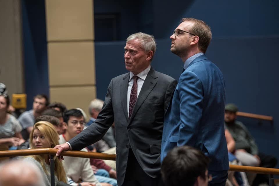 Dominic Fritz in his thirties, standing beside an older man in a suit at a public event
