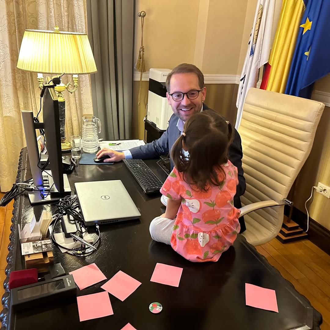 Dominic Fritz working at his desk in the mayor's office, his small daughter sitting on the desk in front of him